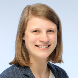 [Translate to Englisch:] Porträt einer Frau mit schulterlangen, dunkelblonden Haaren, weißer Bluse und blauem Sakko.