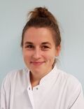 Portraitfoto einer Frau mit braunen Haaren in einem weißen Arztkittel.