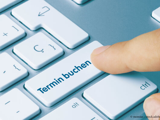 Finger, der auf eine Taste mit der Aufschrift "Termin buchen" auf einer Computertastatur drückt.