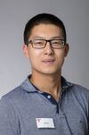 Portraitfoto eines Mannes mit kurzen dunklen Haaren und Brille in einem gestreiften Poloshirt.