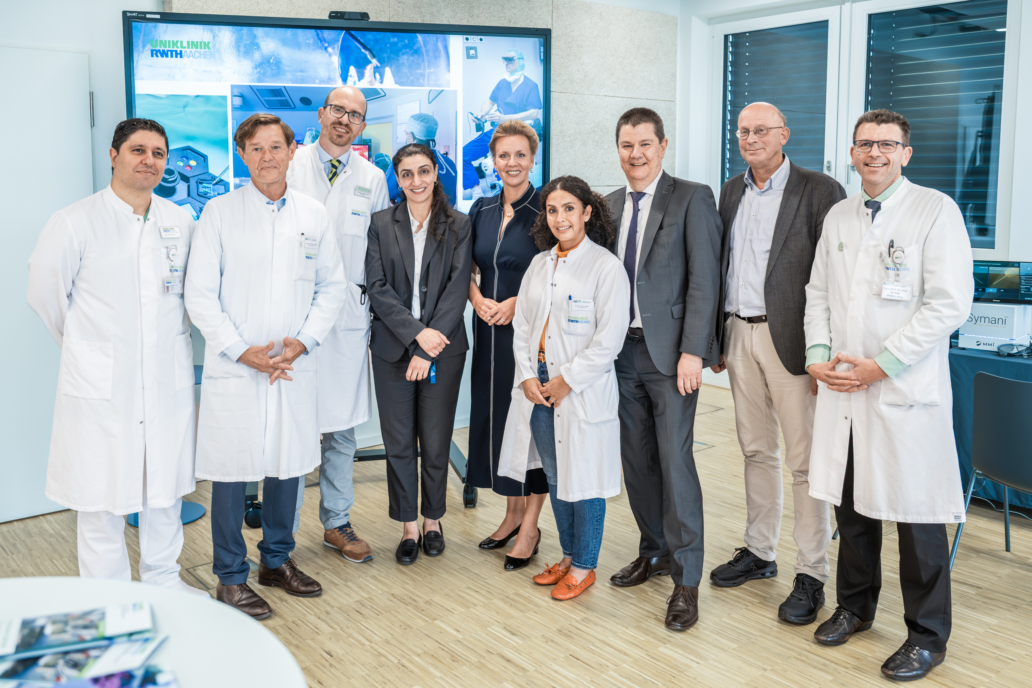 Sechs Männer und drei Frauen, manche in weißen Kitteln und manche in Anzügen, posieren für ein Gruppenbild