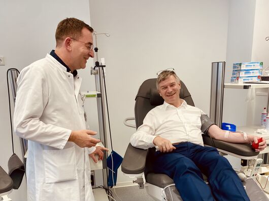 Ein Mann in weißem Hemd liegt auf einer Blutspende-Liege und spendet Blut. 