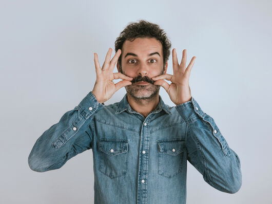 Mann mit Schnurrbart greift diesen an und guckt in die Kamera.