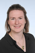 Porträtfoto einer Frau mit schulterlangen, blonden Haaren in einem schwarzen Oberteil. Sie lächelt freundlich in die Kamera. 