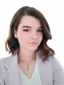 Portraitfoto einer Frau mit schulterlangen braunen Locken in einem hellgrauen Blazer, die freundlich in die Kamera blickt.