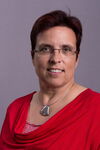Portraitfoto einer Frau mit kurzen roten Haaren und Brille in einem roten Oberteil, die freundlich in die Kamera lächelt. 