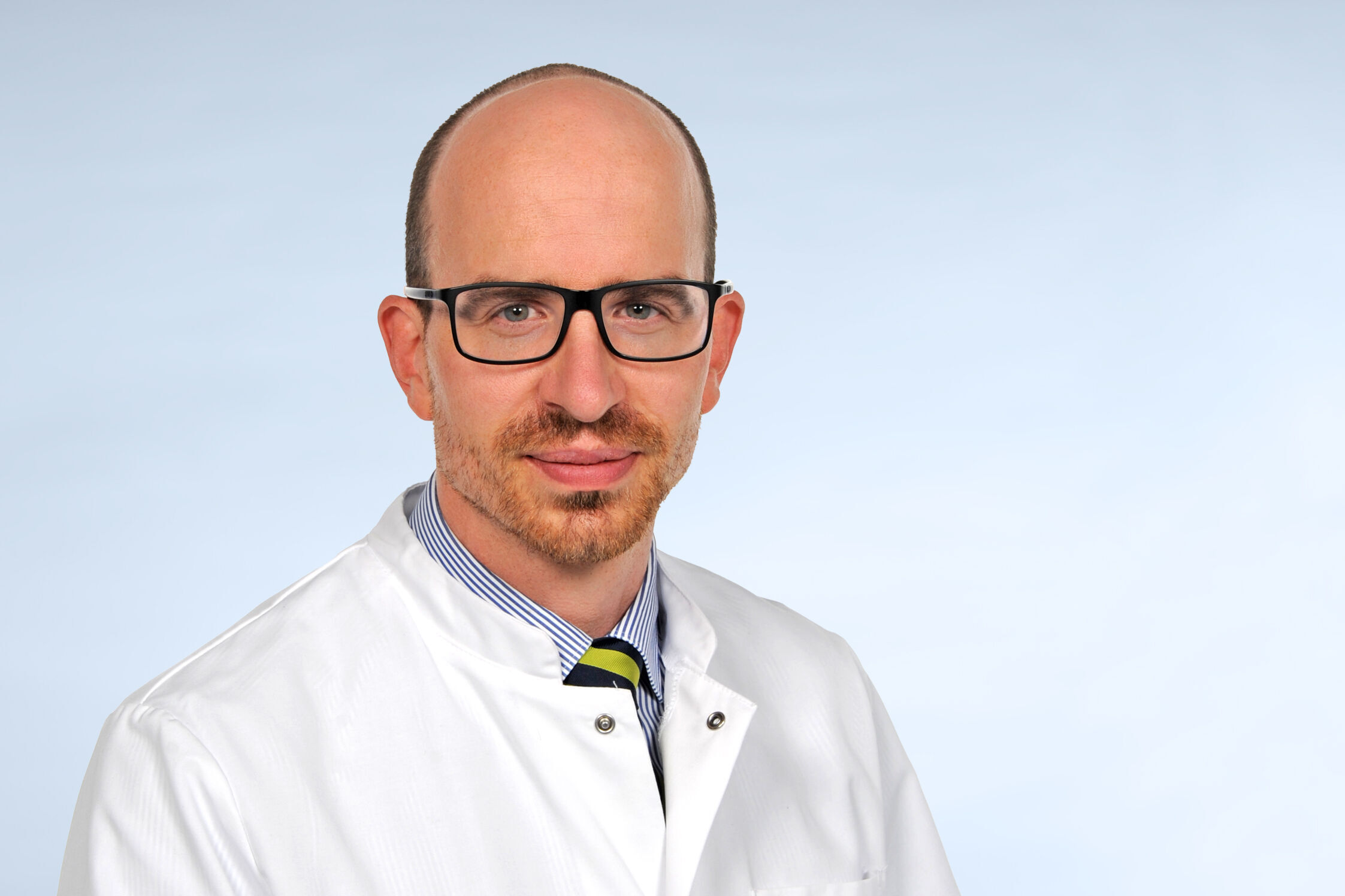 Porträtfoto eines Mannes mit hoher Stirn und einer Brille mit dunklem Brillengestell. Er lächelt freundlich in die Kamera. 