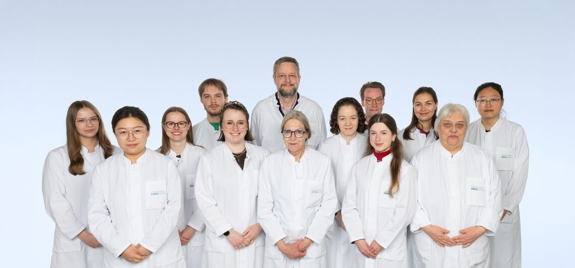 Gruppenfoto von Männern und Frauen in weißen Laborkitteln vor einem hellblauen Hintergrund.
