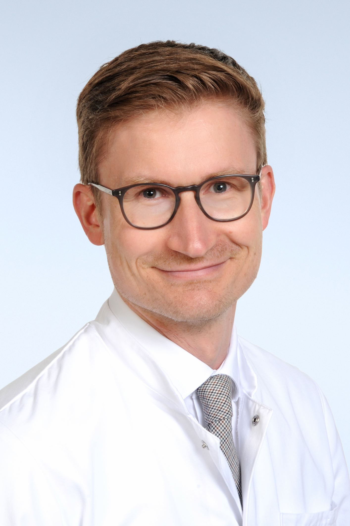 Mann mit Brille, kurzen rot-braunen Haaren, weißen Arztkittel und Krawatte