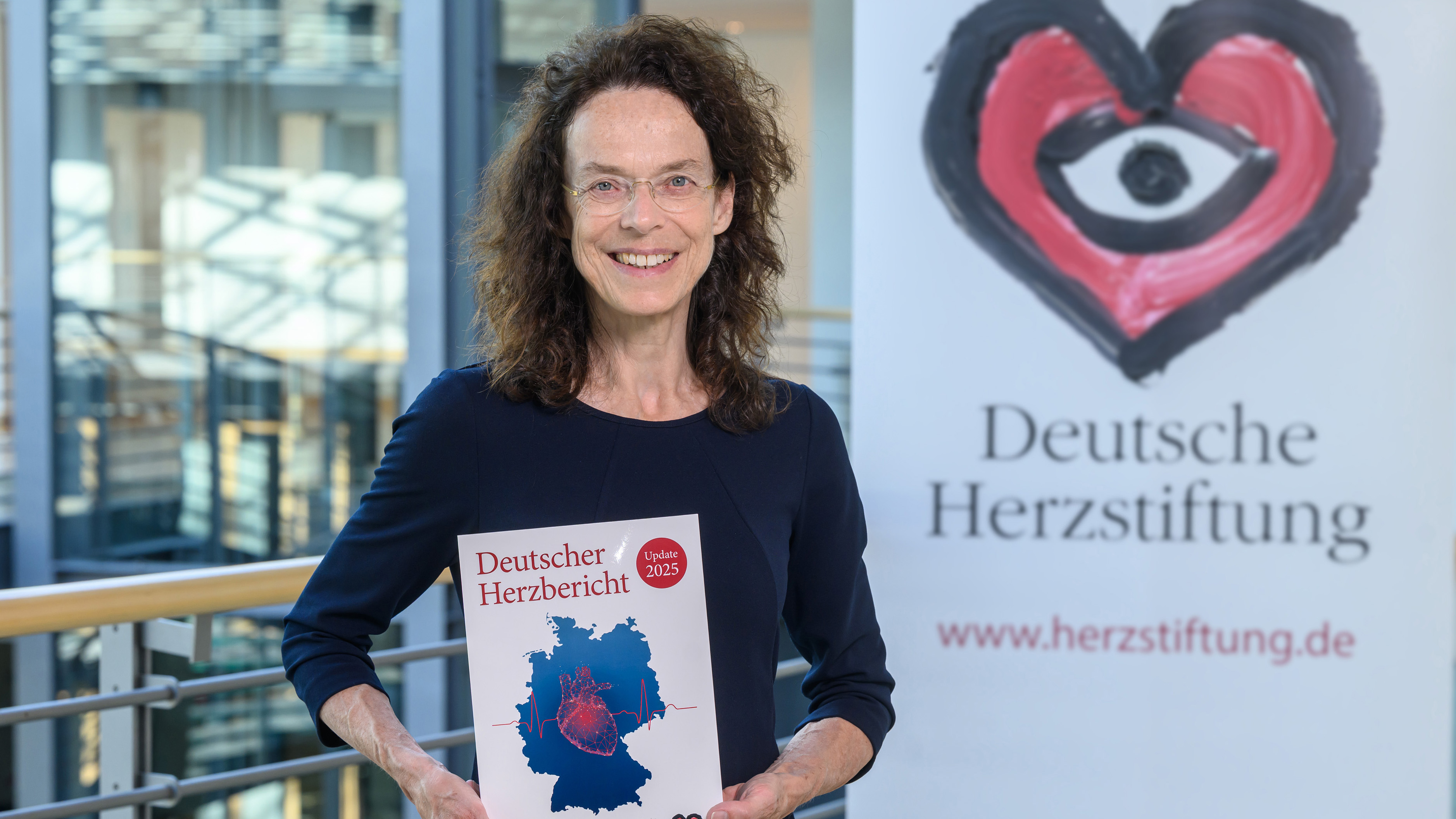 Ältere Frau mit braunen locken und Brille hält den Deutschen Herzbericht 2025 in den Händen