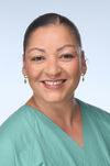 Portraitfoto einer Frau mit braunen hochgebundenen Haaren in einem grünen Kasak, die freundlich in die Kamera lächelt.