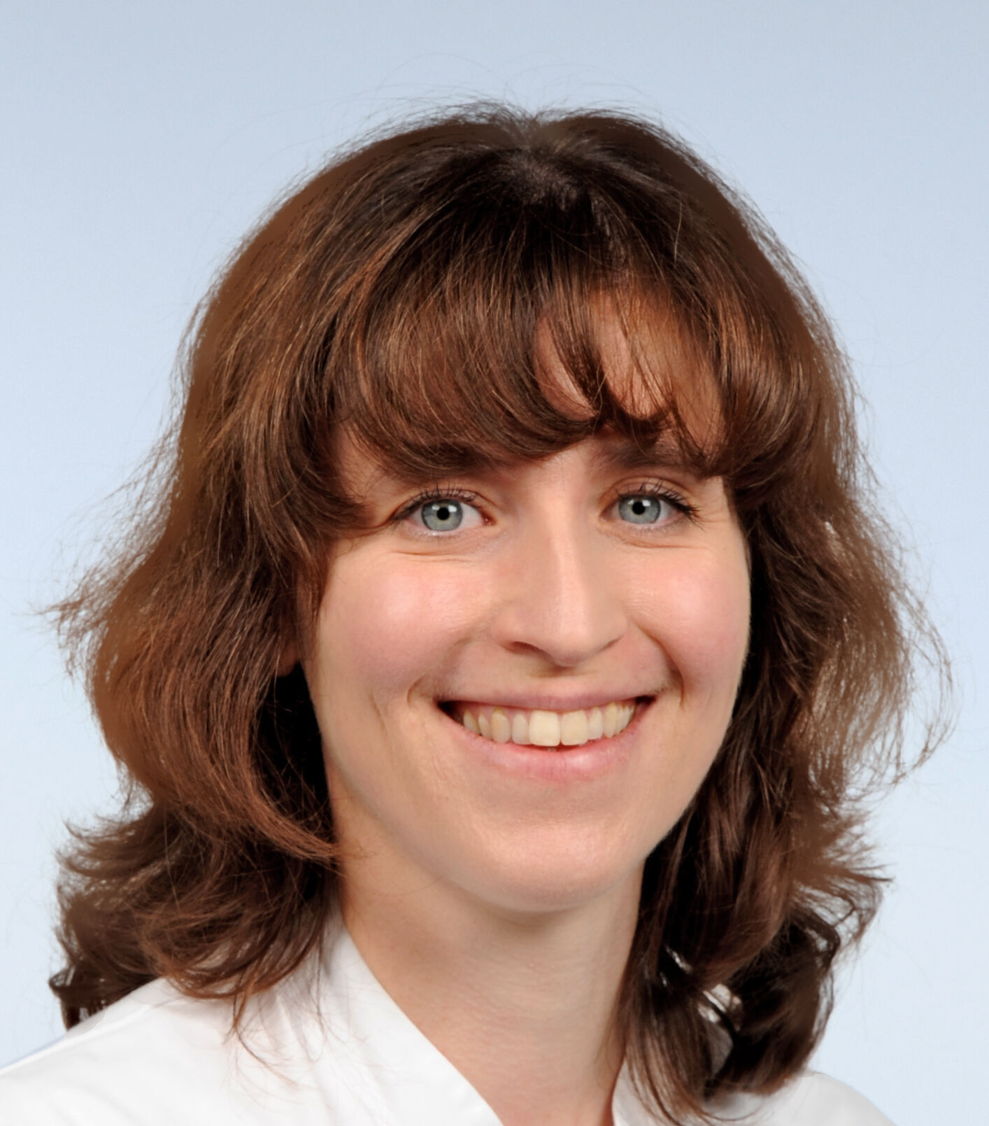 Porträt einer Frau mit schulterlangen rotbraunen Haaren. Sie lächelt und trägt einen weißen Arztkittel.