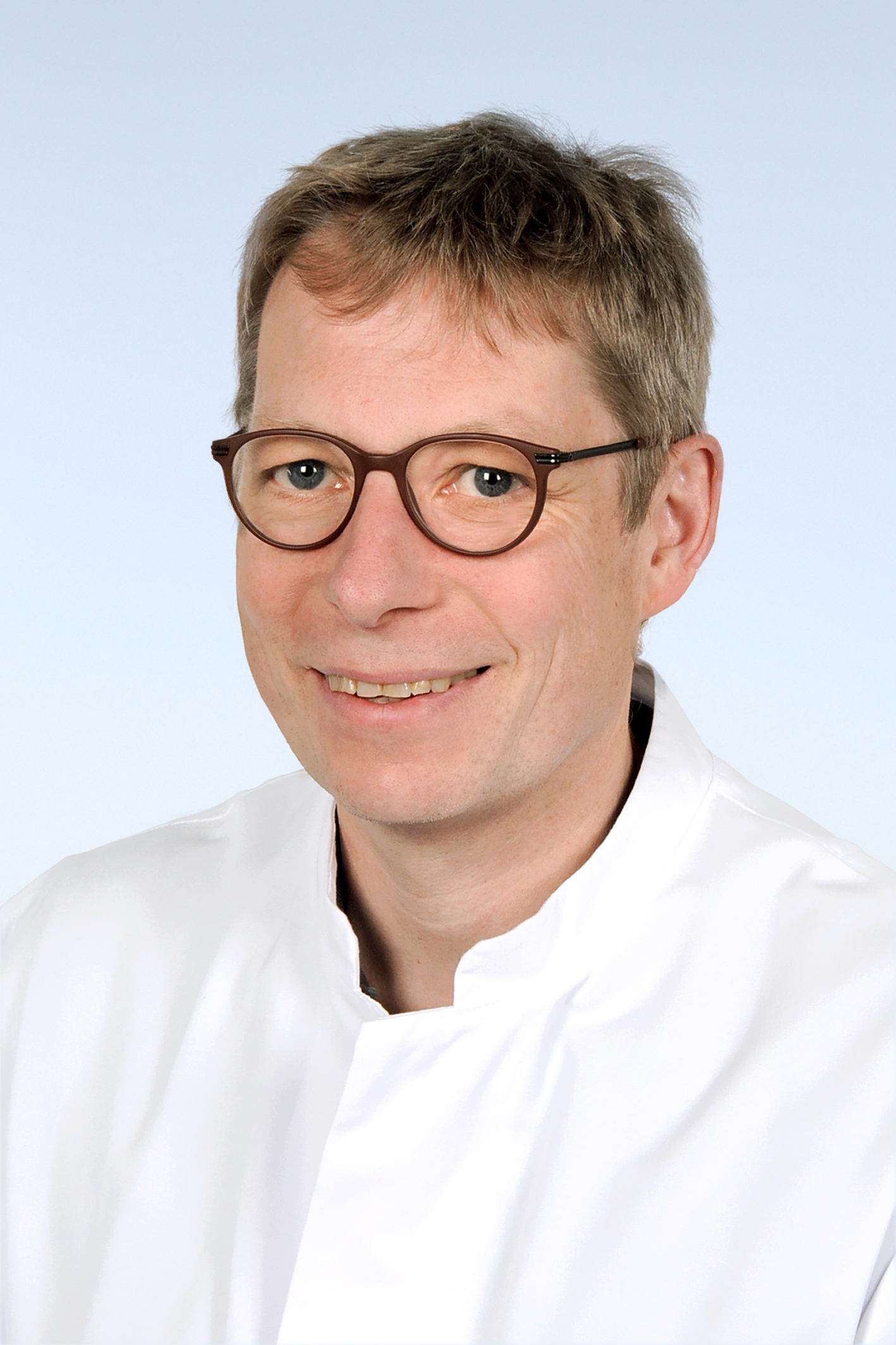 Mann mir Brille im weißen Kittel der freundlich in die Kamera schaut. 