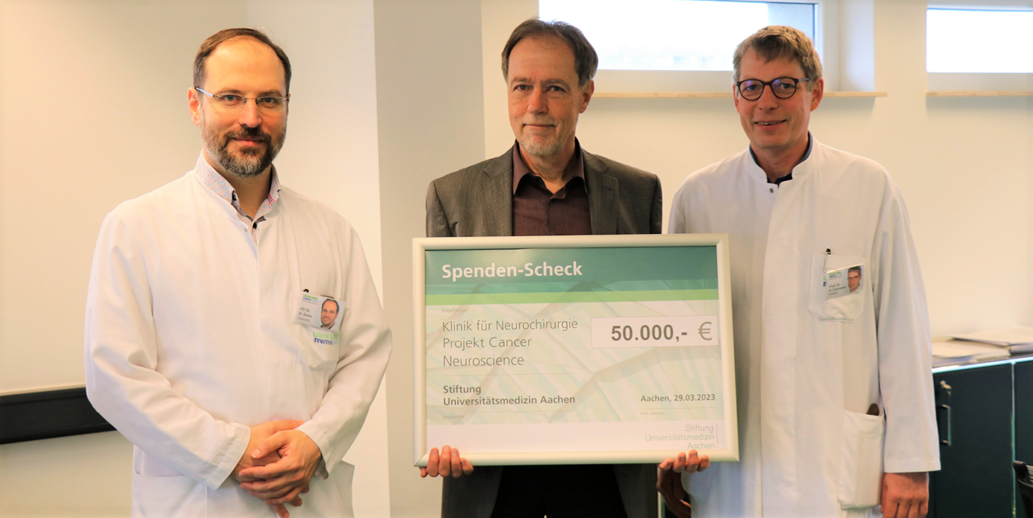 Prof. Thomas H. Ittel, Vorstandsvorsitzender der Uniklinik und der Stiftung Universitätsmedizin Aachen (Mitte), überreicht den Scheck an Priv.-Doz. Dr. med. Daniel Delev (links) und Univ.-Prof. Dr. med. Hans Clusmann, Direktor der Klinik für Neurochirurgie.