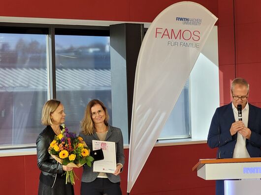 Univ.-Prof. Dr. med. Kathrin Reetz bei der Preisverleihung. Sie hält eine Urkunde iin der Hand und bekommt einen Blumenstrauß überreicht.