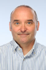 Porträtfoto eines Mannes mit kurzen Haaren. Er trägt ein gestreiftes Hemd.