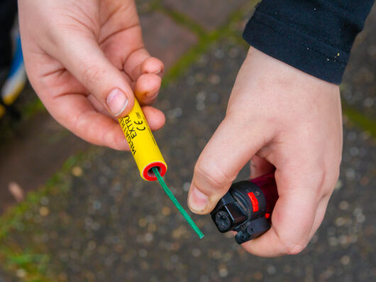 Nahaufnahme von Händen, die einen Böller mit einem Feuerzeug anzünden