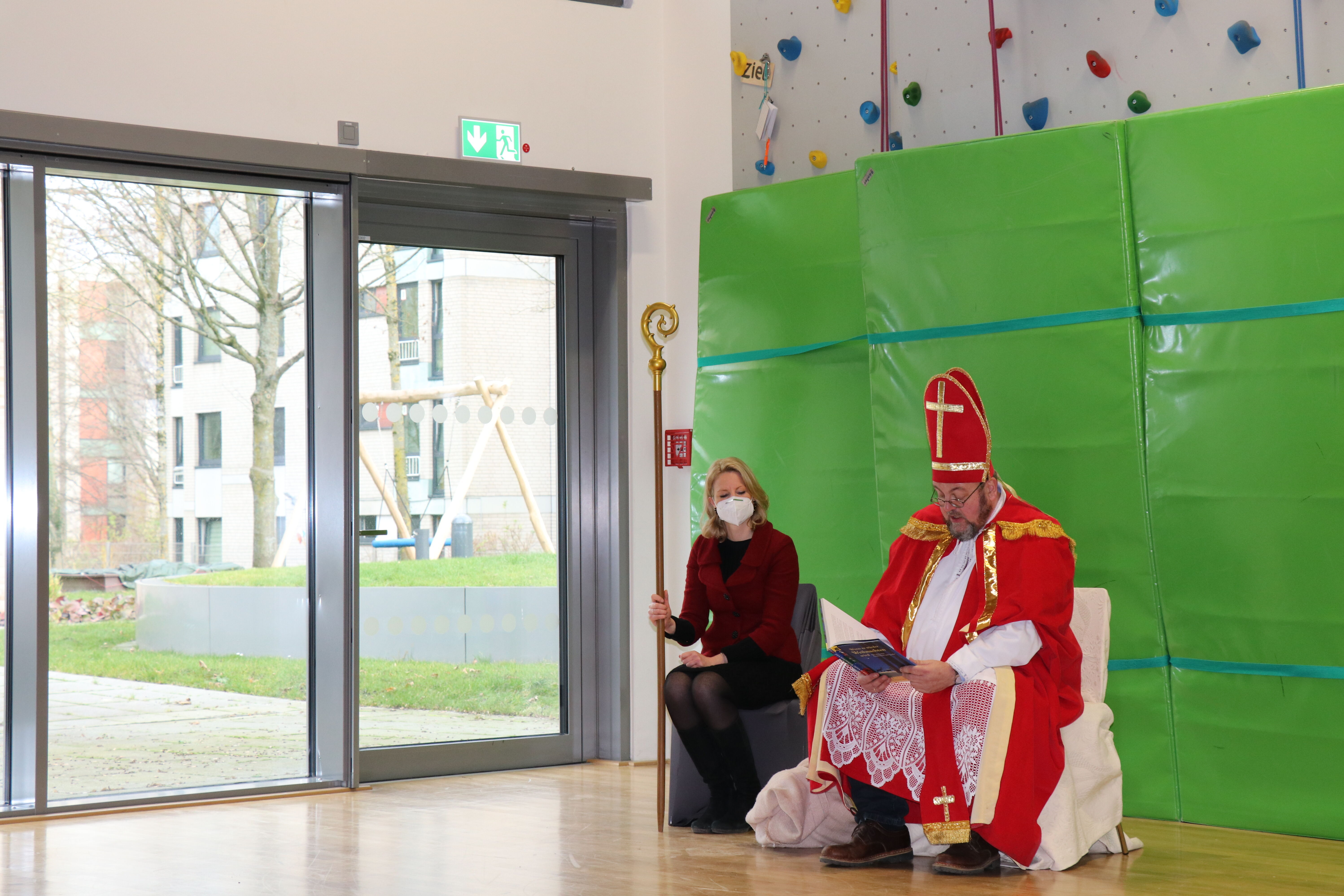 Nikolaus und Knecht Rubrecht sitzen vor einer grünen Kletterwand