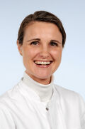 Porträtfoto einer Frau mit braunem Haar und Zopf, die einen weißen Kittel trägt und freundlich in die Kamera lächelt.